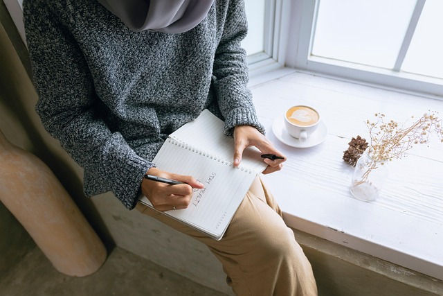 woman sitting on window sill journaling and drinking a cup of tea
