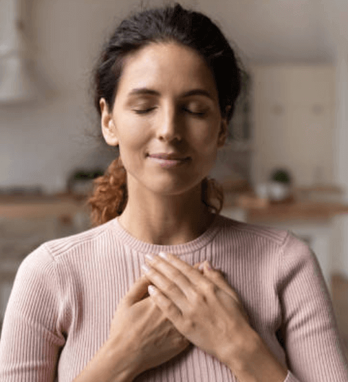 woman with closed eyes and smiling face having both hands on her heart