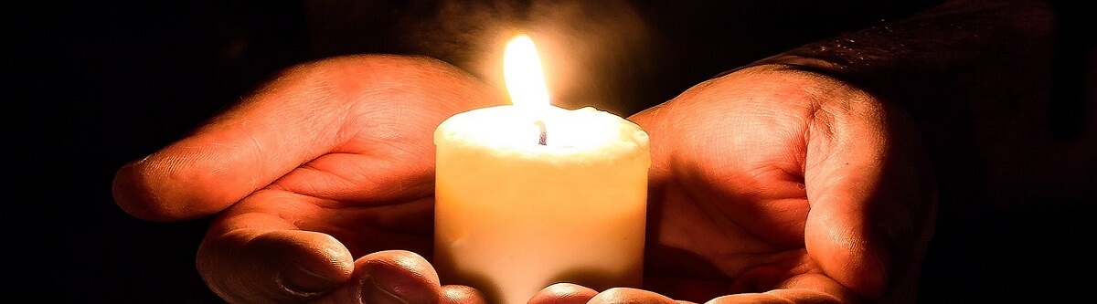 2 cupped hands holding a burning candle